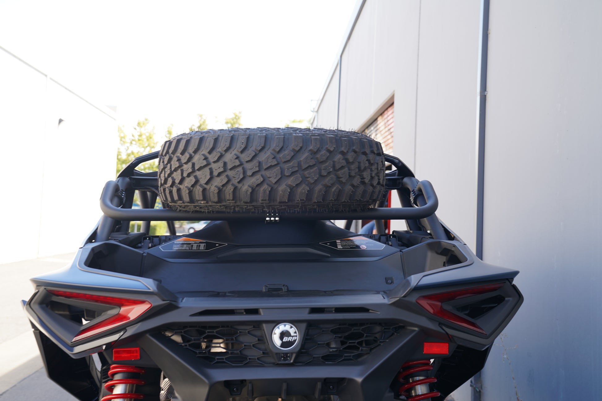 Back view of a vehicle with a spare tire mounted on a rack against a building.