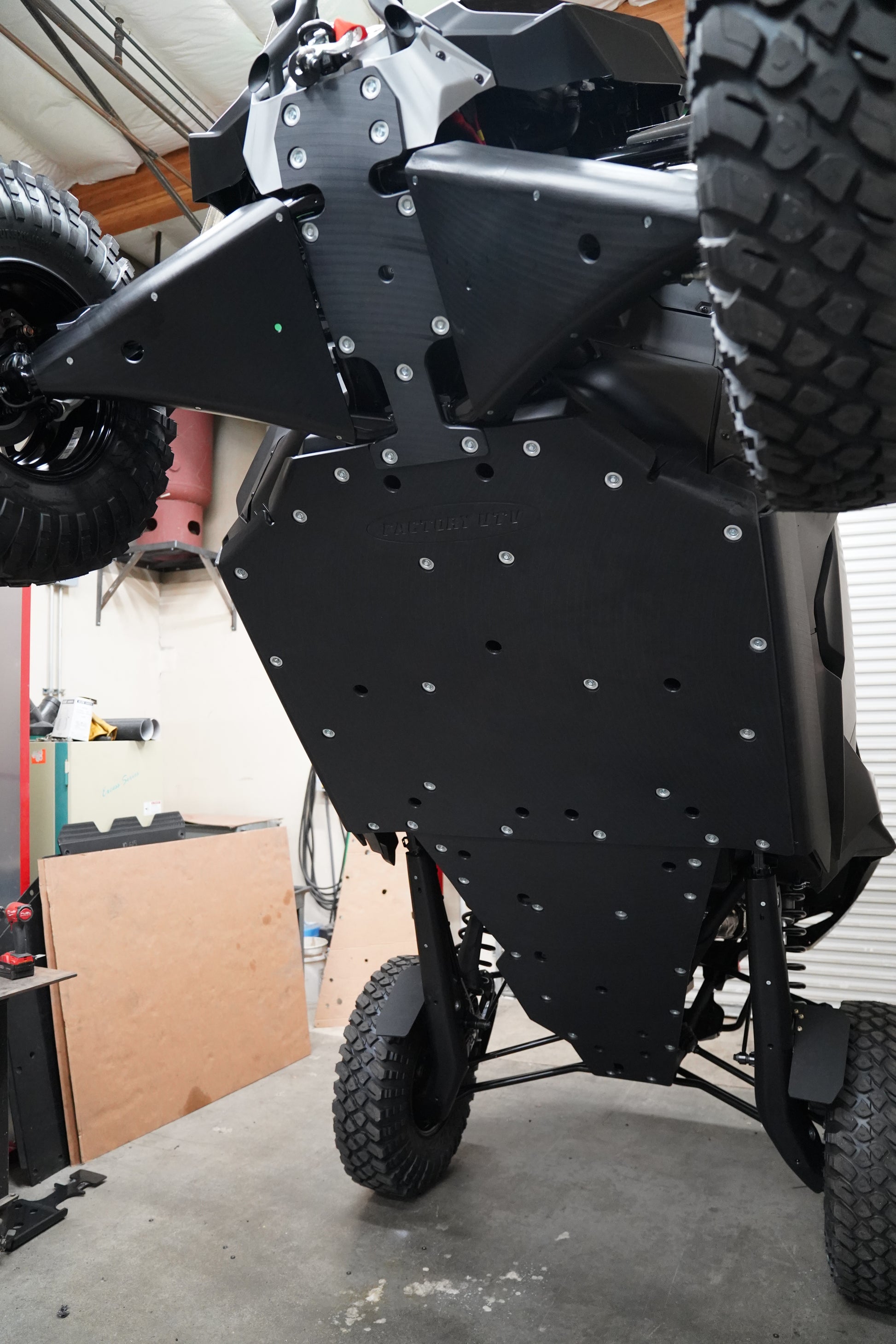 Factory UTV skid plate installation taking place in workshop with vehicle on lift.