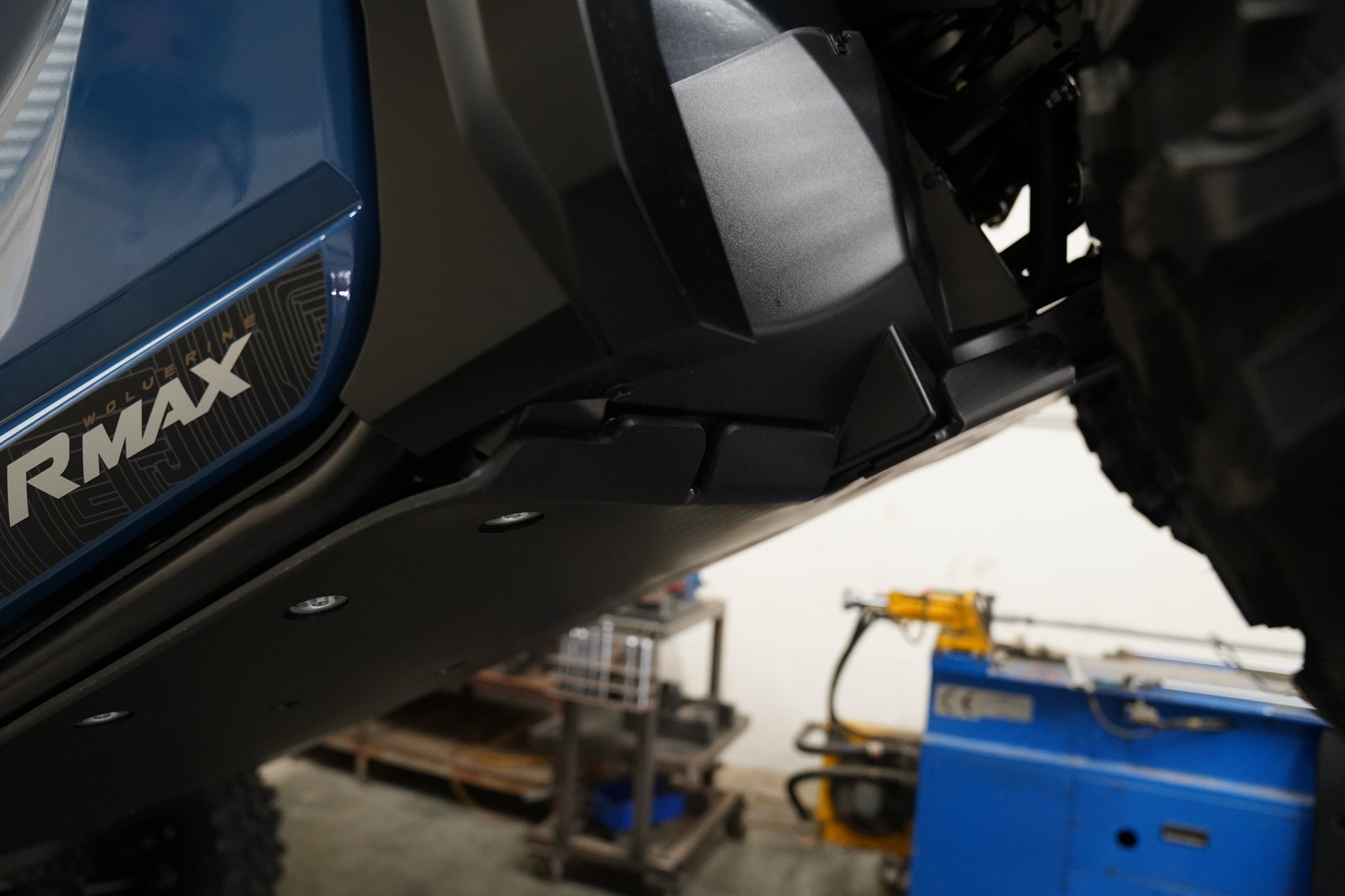 Close-up of a vehicle's undercarriage with 'RMAX' branding in a workshop setting.